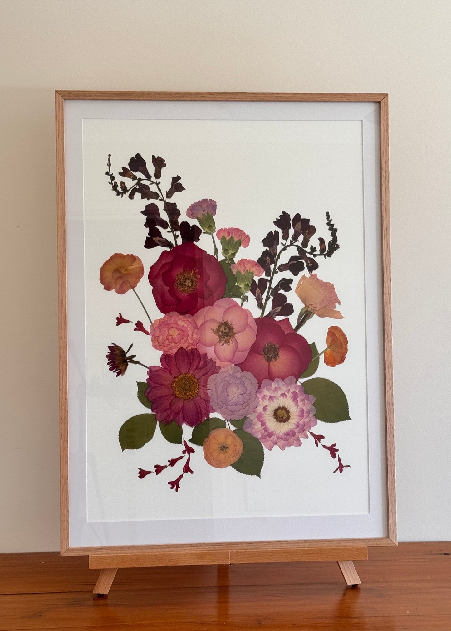 Framed floral print on a wooden stand against a plain wall