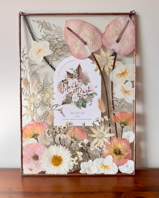 Decorative frame with pressed flowers and a wedding invitation card inside.