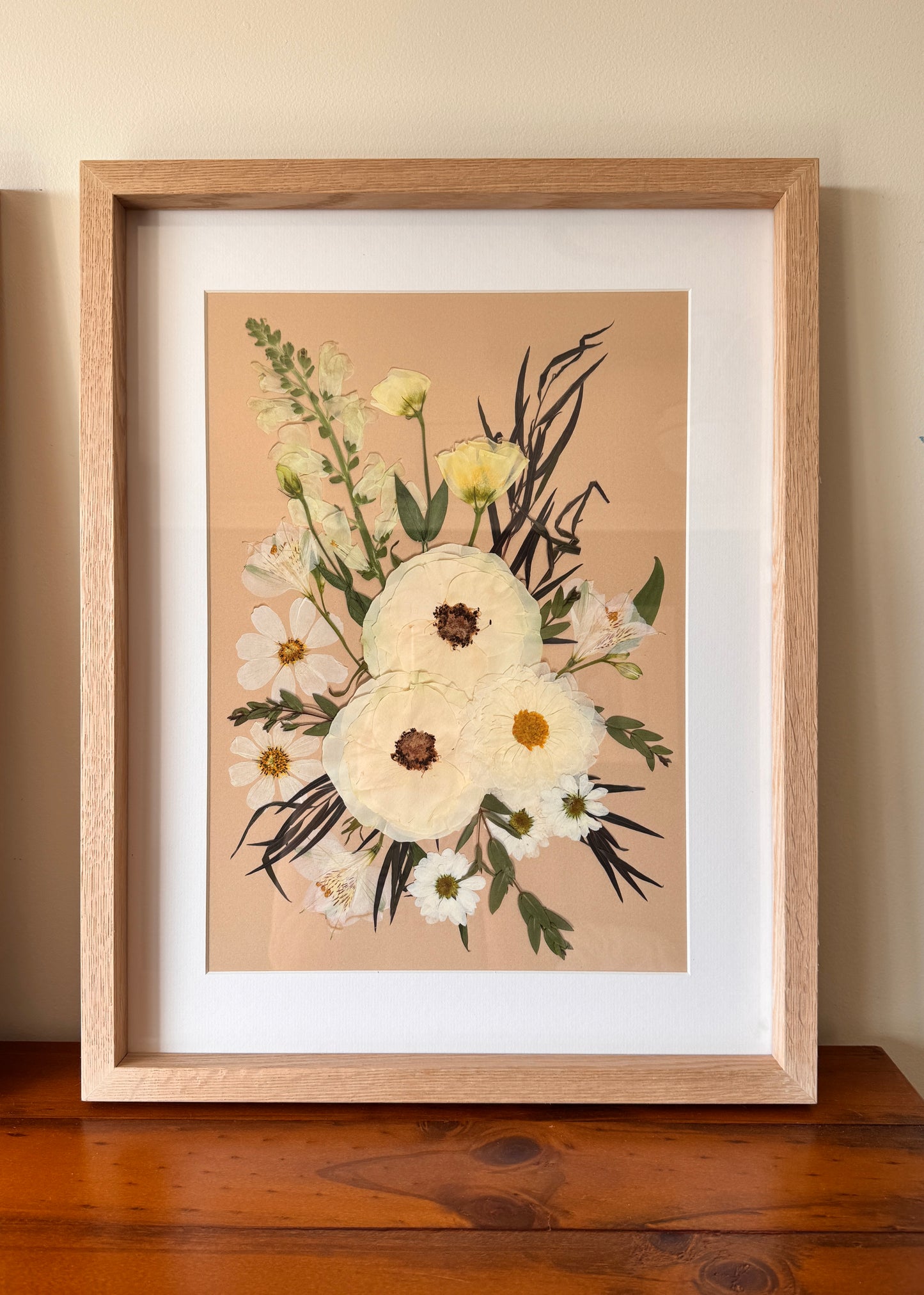 Framed white weddding bouquet on beige background with oak frame