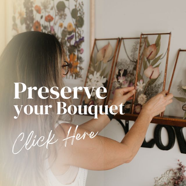 Person arranging framed floral pictures on a wall with text 'Preserve your Bouquet Click Here'.