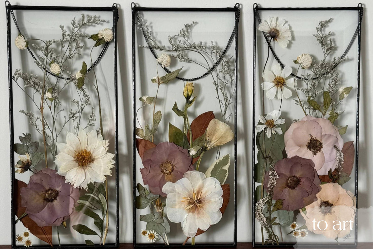 Three panels of pressed flowers with a black frame, featuring a variety of colors and textures.